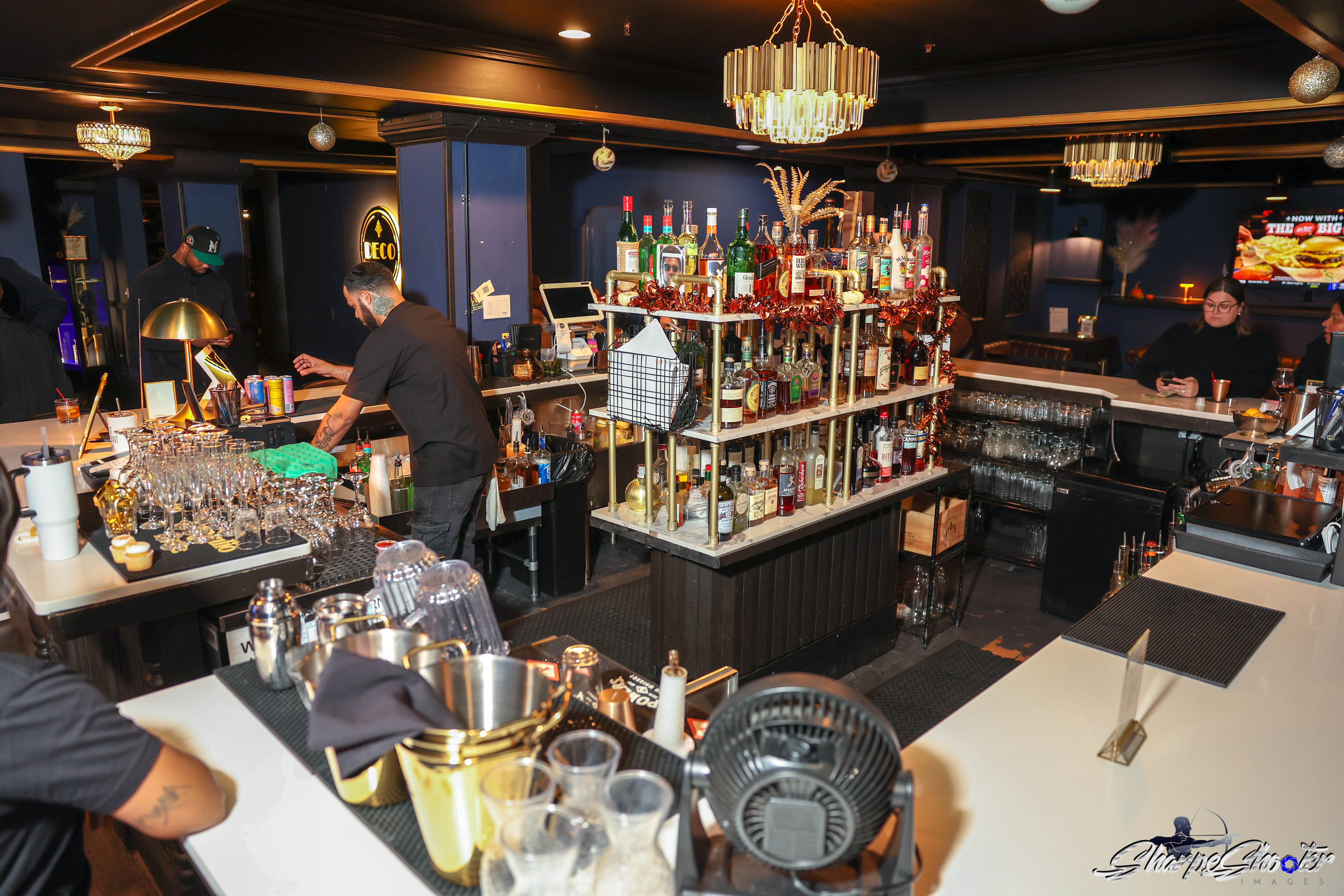 The Deco bar island with its brass bottle display beneath a crystal chandelier
